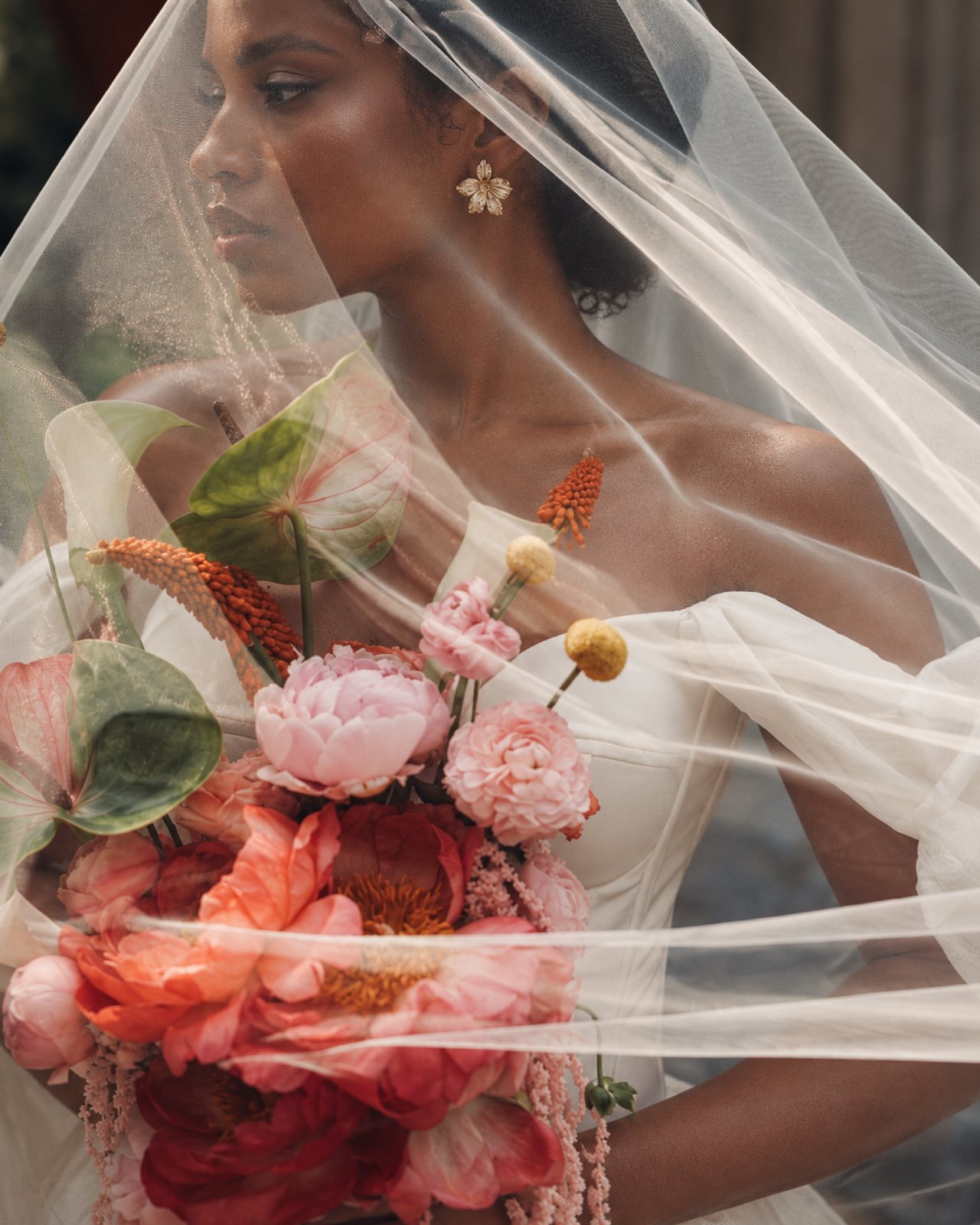 Bride beneath a veil holding a vibrant bouquet